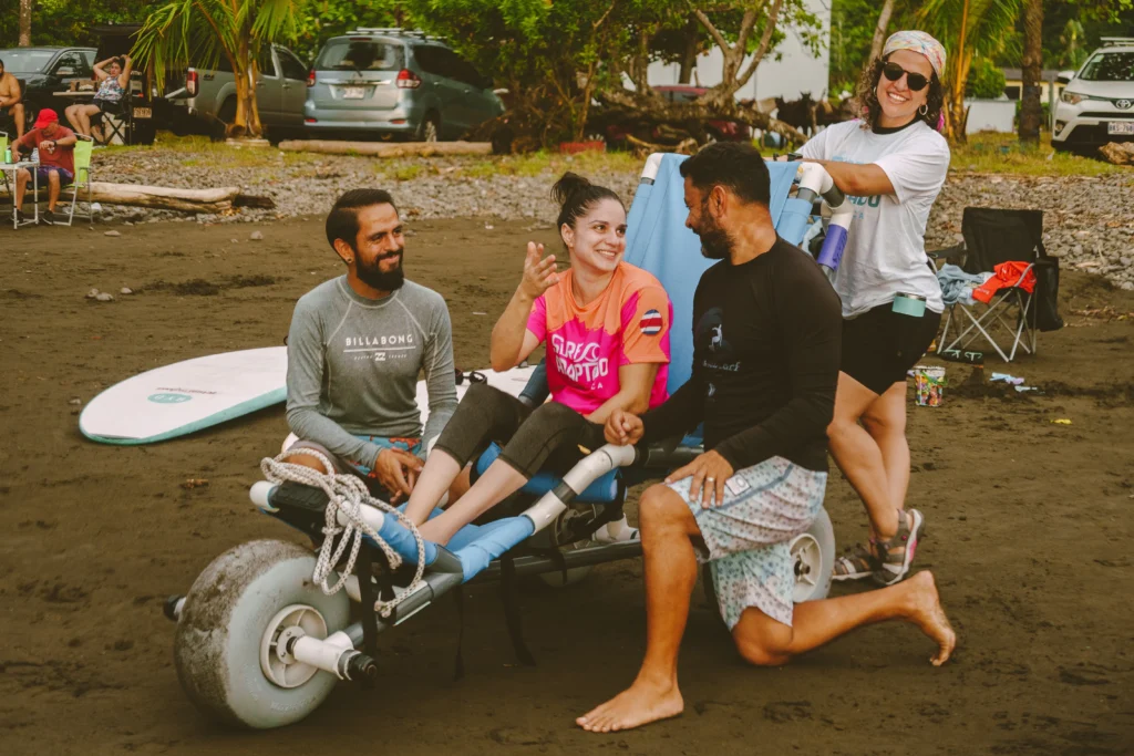 Persona en silla anfibia hablando con instructor de surf y acompañados de voluntarios