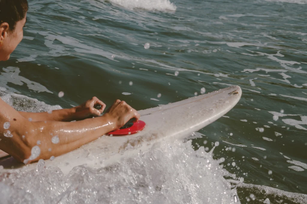 Mujer surfeando prone en tabla con agarraderas
