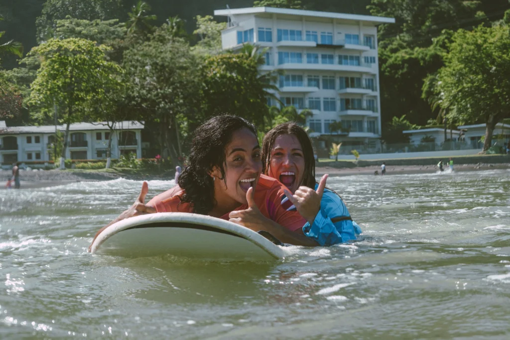 Mujer en tabla con instructora detrás viendo a la camara y sonriendo